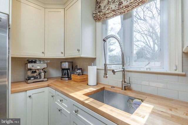 kitchen with wooden counters, backsplash, stainless steel fridge, and a sink