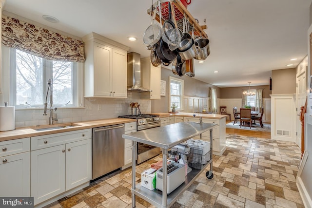 kitchen featuring stone tile floors, wall chimney exhaust hood, a peninsula, stainless steel appliances, and a sink