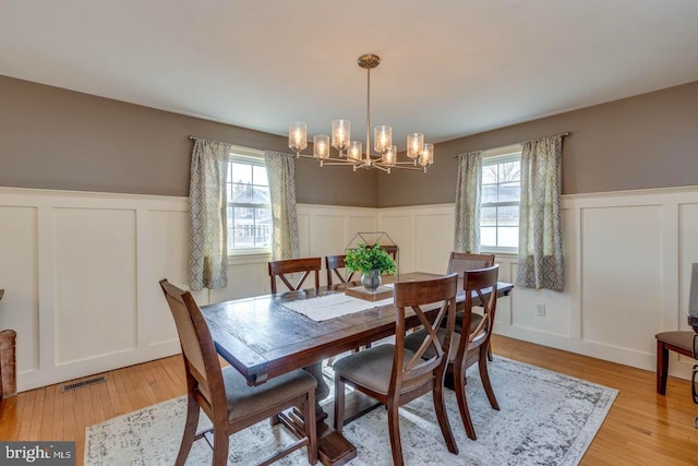 dining area with light wood-style floors, visible vents, a chandelier, and wainscoting