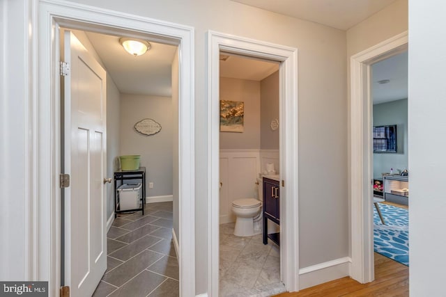 bathroom featuring toilet, a wainscoted wall, a decorative wall, and vanity