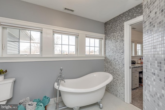 full bath with toilet, a soaking tub, visible vents, and tile patterned floors