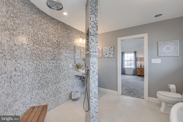 bathroom with toilet, tile patterned flooring, baseboards, and a tile shower