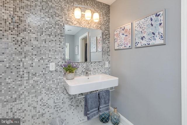 bathroom featuring tile walls, baseboards, decorative backsplash, and a sink