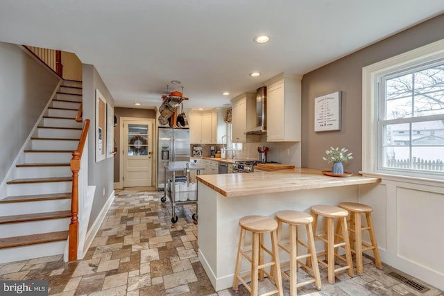 kitchen featuring visible vents, decorative backsplash, wall chimney exhaust hood, stone finish floor, and stainless steel appliances