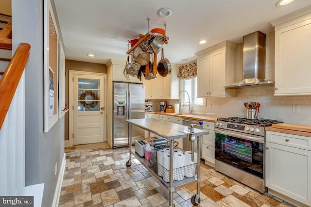 kitchen featuring appliances with stainless steel finishes, wall chimney range hood, stone tile flooring, and tasteful backsplash