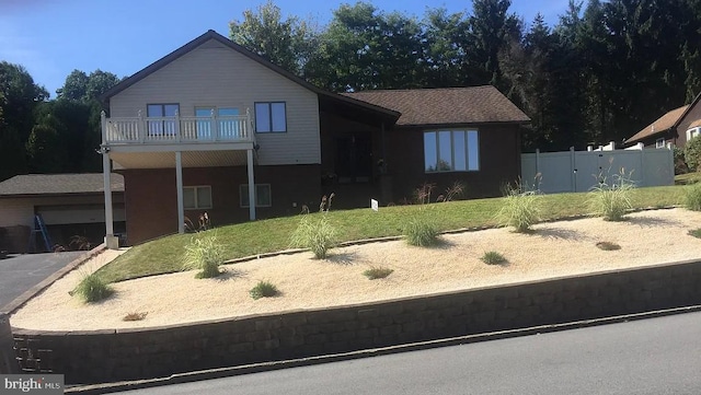 view of front of property featuring a balcony, fence, aphalt driveway, and a front yard