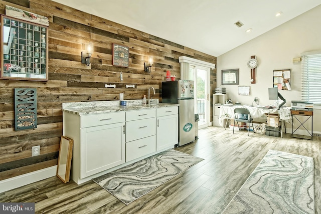 interior space with wooden walls, wood finished floors, visible vents, vaulted ceiling, and freestanding refrigerator