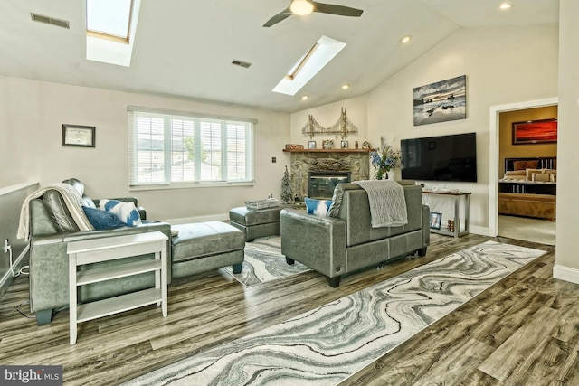 living room with lofted ceiling with skylight, a fireplace, visible vents, and wood finished floors