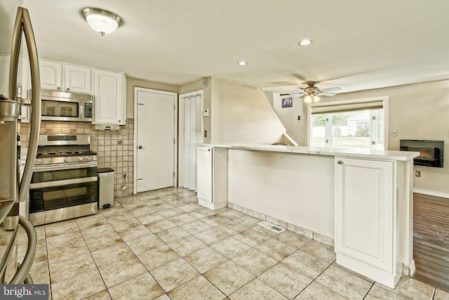 kitchen featuring stainless steel appliances, light countertops, a ceiling fan, white cabinetry, and a peninsula