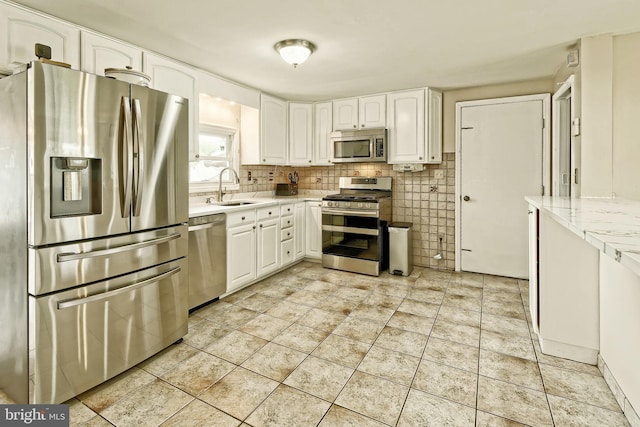 kitchen featuring white cabinets, light stone counters, appliances with stainless steel finishes, a sink, and backsplash