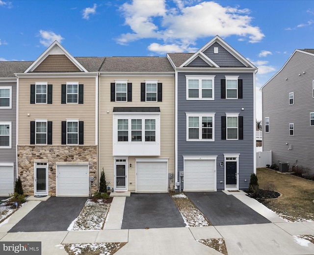 multi unit property featuring a garage, stone siding, central AC unit, and driveway