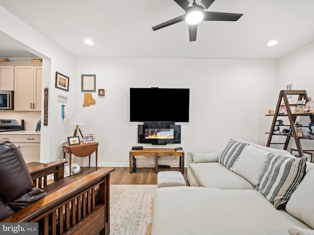 living area featuring a ceiling fan, a glass covered fireplace, wood finished floors, recessed lighting, and baseboards