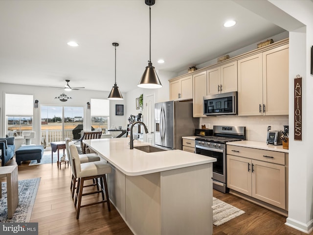 kitchen with a sink, light countertops, appliances with stainless steel finishes, dark wood-style floors, and a kitchen island with sink