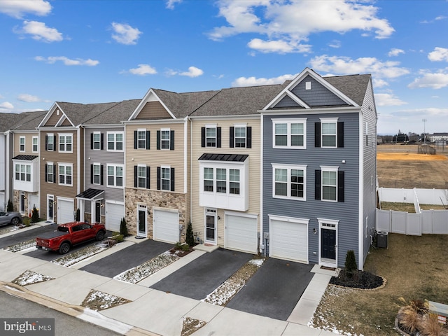 multi unit property with fence, driveway, central AC, a garage, and stone siding