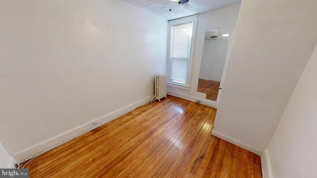 spare room with radiator, light wood-style floors, and baseboards