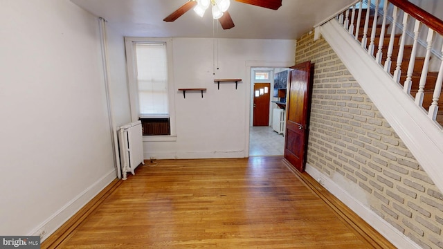 corridor featuring stairway, radiator heating unit, brick wall, light wood-type flooring, and baseboards