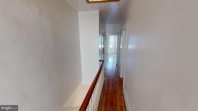 hall featuring dark wood-style floors, baseboards, and an upstairs landing