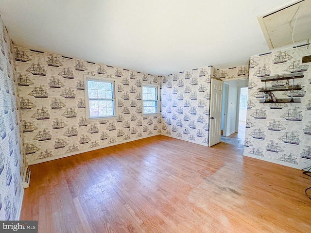 spare room featuring attic access, wood finished floors, baseboards, and wallpapered walls