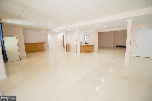 finished basement featuring a drop ceiling, fridge, and baseboards