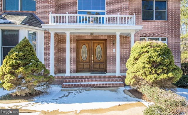 view of exterior entry with brick siding and a balcony