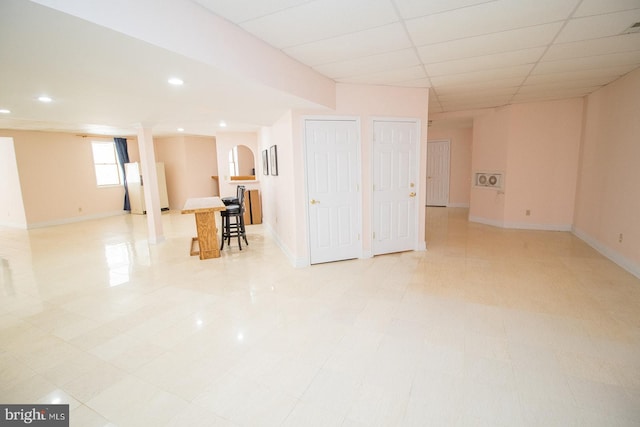 basement featuring freestanding refrigerator, a drop ceiling, baseboards, and recessed lighting