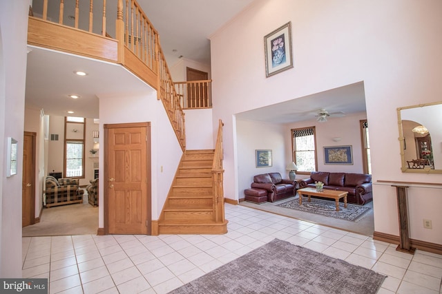 entryway featuring baseboards, a ceiling fan, a towering ceiling, stairway, and light tile patterned flooring