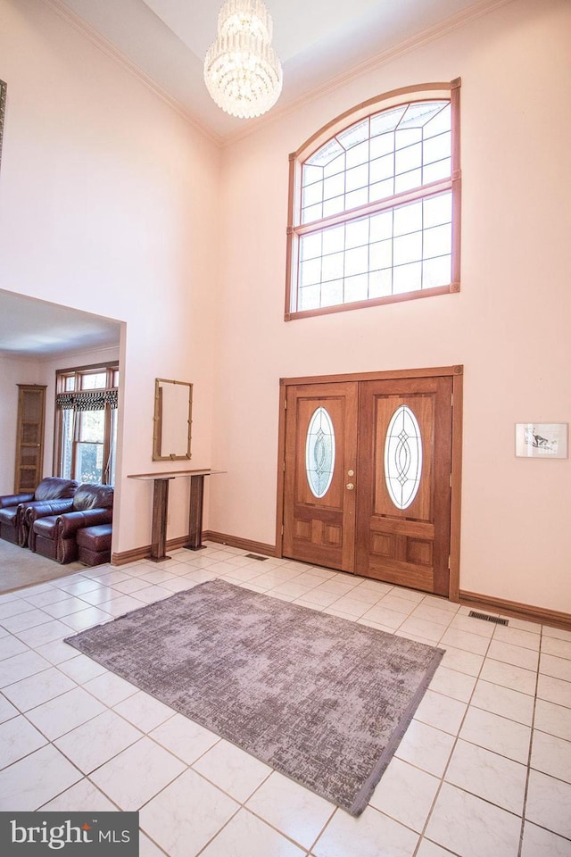 foyer entrance featuring light tile patterned floors, ornamental molding, visible vents, and an inviting chandelier