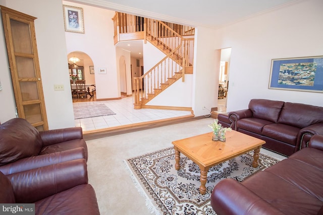 carpeted living area with arched walkways, crown molding, baseboards, and stairs