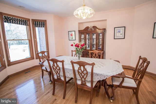 dining space with baseboards, visible vents, light wood-style flooring, crown molding, and a notable chandelier