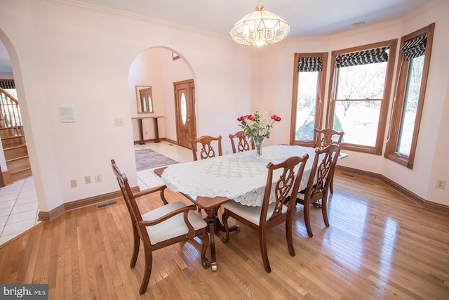 dining area with arched walkways, ornamental molding, stairs, and light wood-style flooring