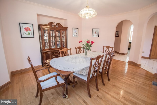 dining area with arched walkways, light wood-type flooring, baseboards, and crown molding