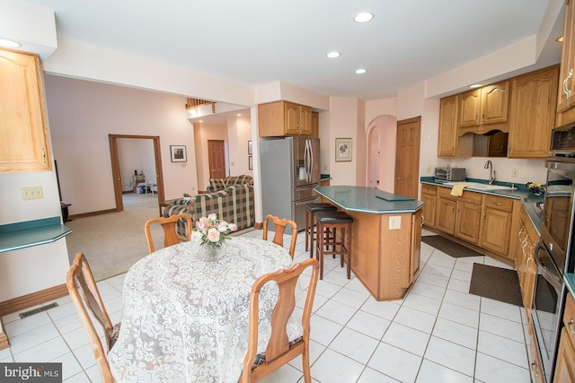 kitchen featuring visible vents, dark countertops, a kitchen island, stainless steel refrigerator with ice dispenser, and a sink