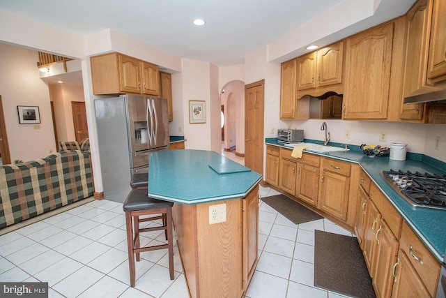 kitchen with light tile patterned floors, arched walkways, appliances with stainless steel finishes, a center island, and a sink