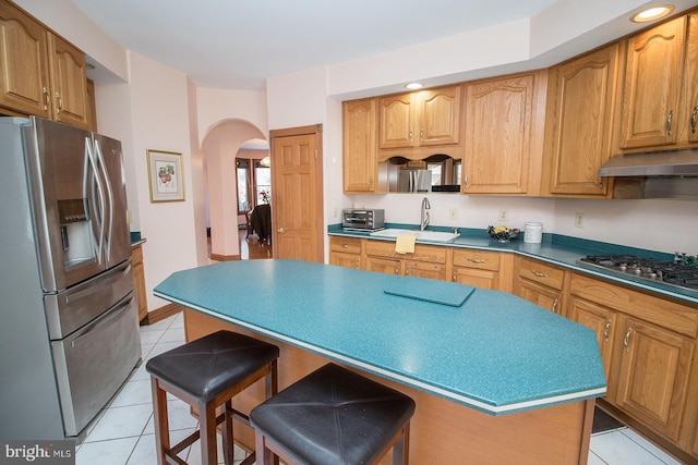 kitchen with arched walkways, under cabinet range hood, a kitchen island, appliances with stainless steel finishes, and a kitchen bar