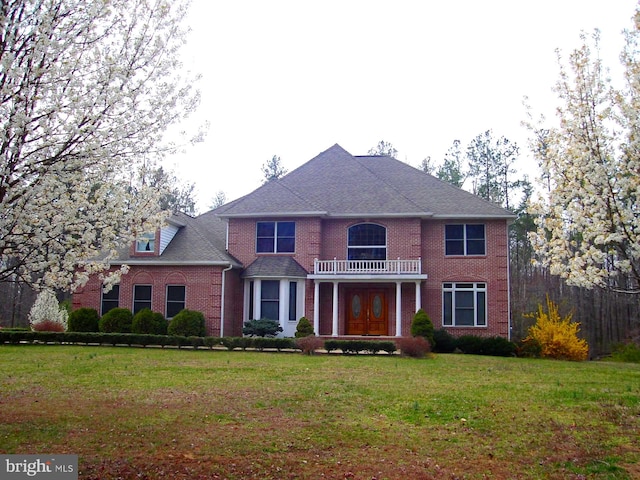 georgian-style home featuring brick siding, a balcony, and a front lawn