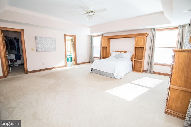 unfurnished bedroom featuring light carpet, baseboards, a raised ceiling, and a ceiling fan