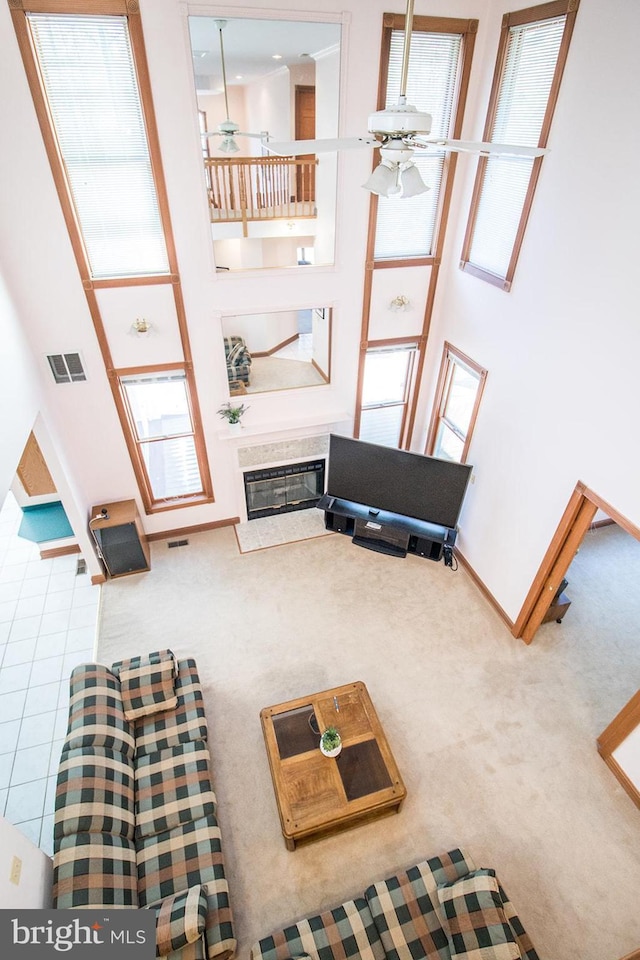 carpeted living room featuring visible vents, a towering ceiling, a high end fireplace, ceiling fan, and baseboards