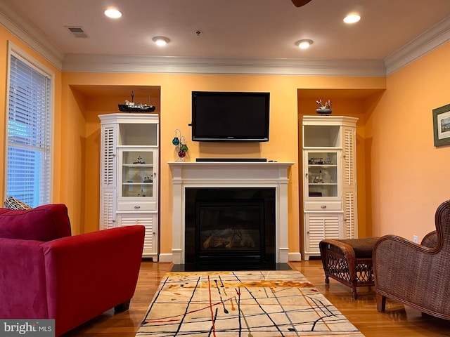 living room with crown molding, recessed lighting, visible vents, a fireplace with flush hearth, and wood finished floors