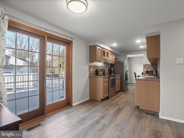 kitchen with dark countertops, light wood-style flooring, stainless steel appliances, and decorative backsplash