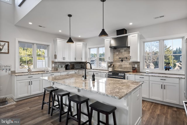 kitchen featuring dark wood-style floors, visible vents, high end stainless steel range oven, a sink, and wall chimney exhaust hood