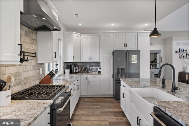 kitchen with visible vents, white cabinets, wall chimney exhaust hood, appliances with stainless steel finishes, and a sink