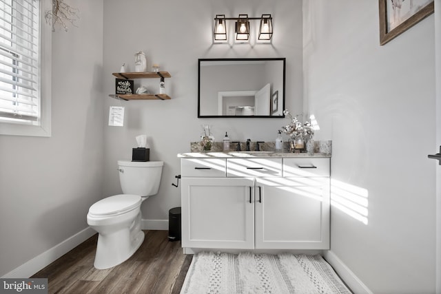 half bath featuring baseboards, vanity, toilet, and wood finished floors