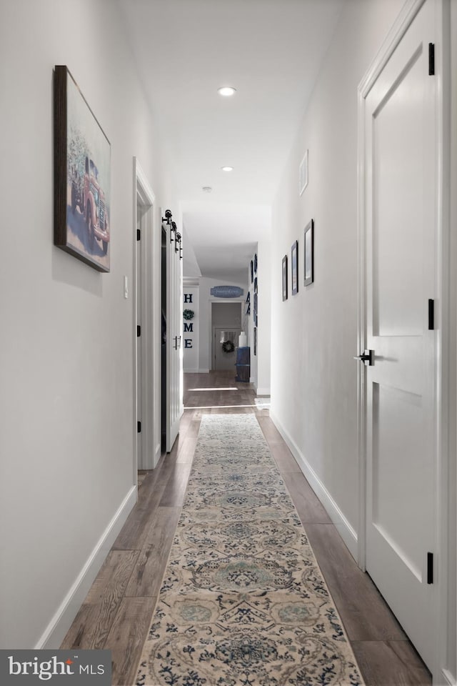 hall featuring a barn door, wood finished floors, visible vents, and baseboards