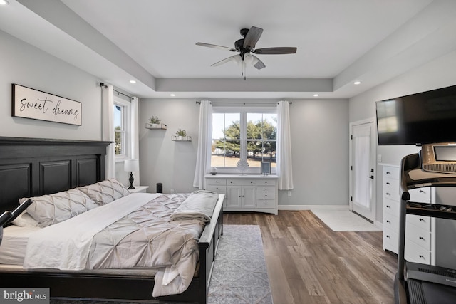 bedroom with baseboards, a raised ceiling, wood finished floors, and recessed lighting