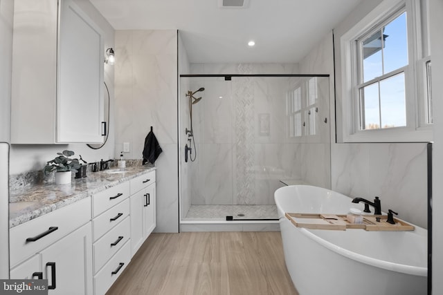 bathroom with tile walls, a soaking tub, vanity, and a marble finish shower