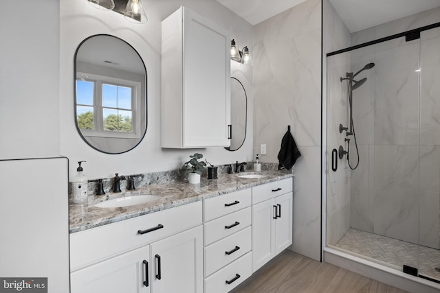 bathroom with double vanity, wood finished floors, a sink, and a shower stall