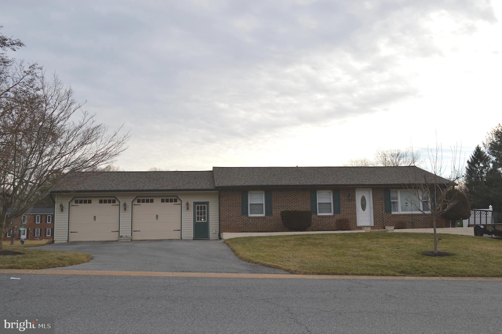 single story home featuring a garage, brick siding, driveway, and a front lawn