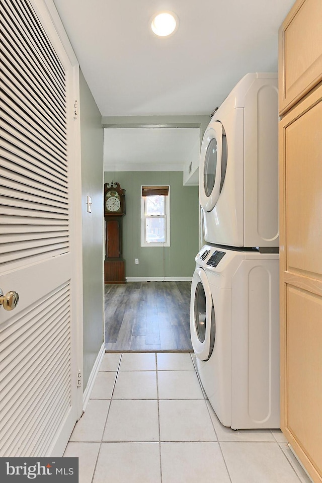 clothes washing area featuring light tile patterned floors, baseboards, cabinet space, and stacked washer and clothes dryer