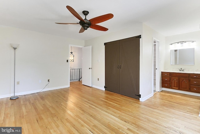 unfurnished bedroom with baseboards, light wood-type flooring, ensuite bathroom, and a sink