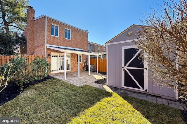 rear view of house with a shed, a yard, a fenced backyard, french doors, and brick siding